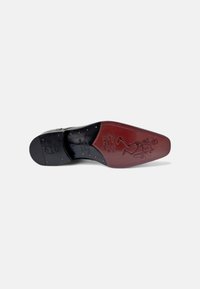 Suela de zapato de cuero negro con acentos rojos. Presenta un diseño en relieve de un esqueleto, costuras decorativas y tachuelas metálicas a lo largo del borde.