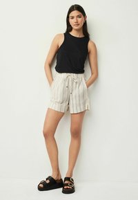 Débardeur noir sans manches associé à un short rayé beige clair. Le short a une taille avec cordon de serrage et des poches latérales. Sandales à plateforme noires.