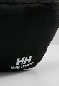 Sac en tissu noir présentant une texture lisse, une forme arrondie et un logo blanc Helly-Hansen bien visible avec les initiales "HH".