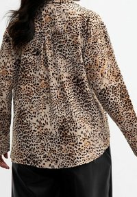 Košile na knoflíky z měkké látky s krémovým leopardím potiskem, dlouhými rukávy, zadními vsadkami a volnějším střih. Lem je zakřivený.