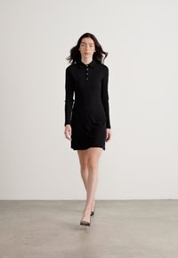 Zwart langemouwen jurk met een kraag en knoopsluiting. Glad, elastisch materiaal, getailleerde pasvorm, eindigend boven de knie.
