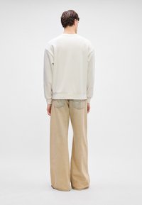 Κρέμα φούτερ με ρίγες στους ώμους, συνδυασμένο με φαρδιά ανοιχτό μπεζ παντελόνια που διαθέτουν πίσω τσέπες και ήπια υφή.