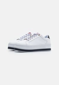 Sneakers bianchi in pelle con suola nera spessa, caratterizzati da occhielli dorati e lacci multicolori. Testura resistente e liscia, design sportivo.