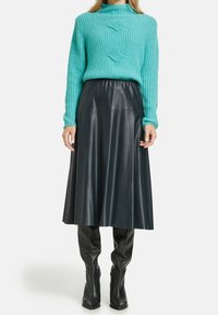 Maglione turchese lavorato a maglia con scollatura alta, abbinato a una gonna midi in pelle nera e stivali neri fino al ginocchio. Materiali strutturati e lisci.