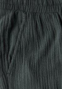 Dark green, textured fabric with vertical pleats. Elastic waistband and side pockets, showcasing a soft, wrinkled appearance.
