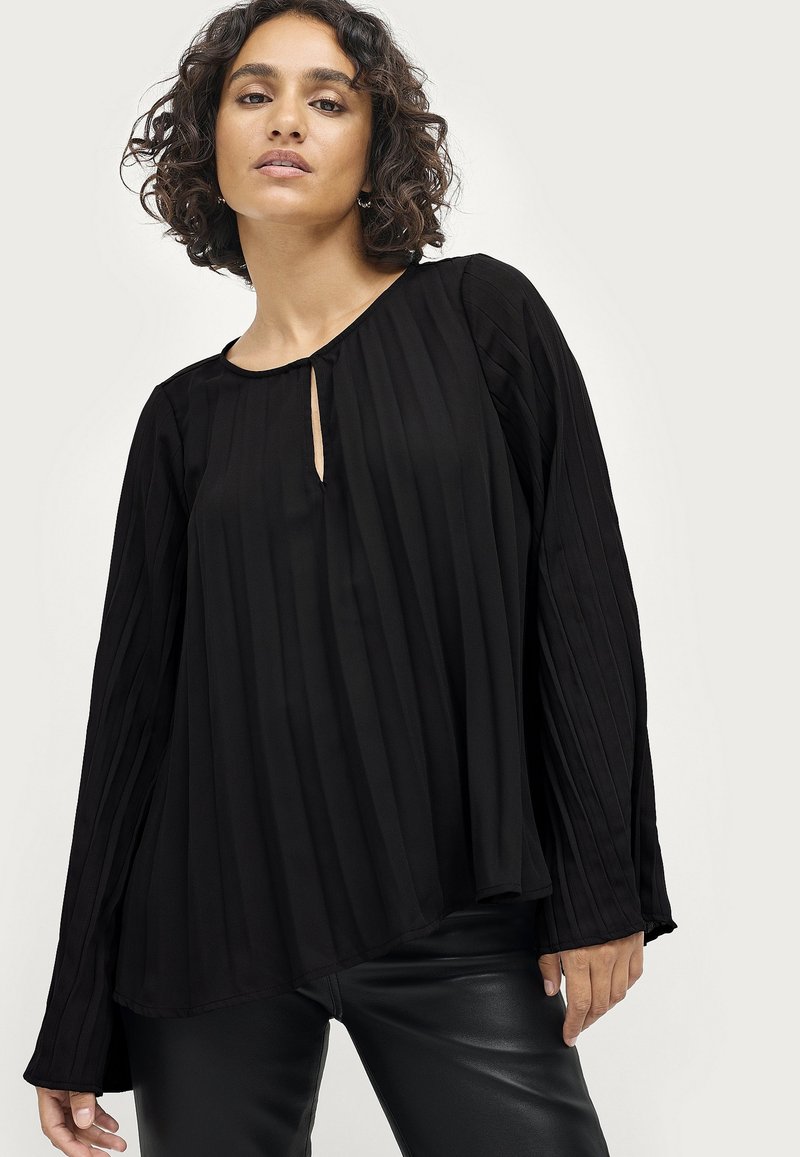 Schwarze plissierte Bluse mit rundem Ausschnitt, Schlitzdetail vorne und langen, ausgestellten Ärmeln; weicher Stoff mit glatter Textur.