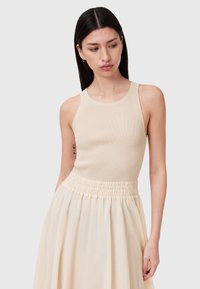 Top in cotone beige a coste con scollo rotondo, abbinato a una gonna pesca con vita arricciata realizzata in tessuto leggero.