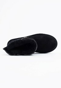 Botín negro de tobillo hecho de suave ante, con un interior acolchado y una punta redondeada. Detalle de cremallera lateral para un fácil uso.