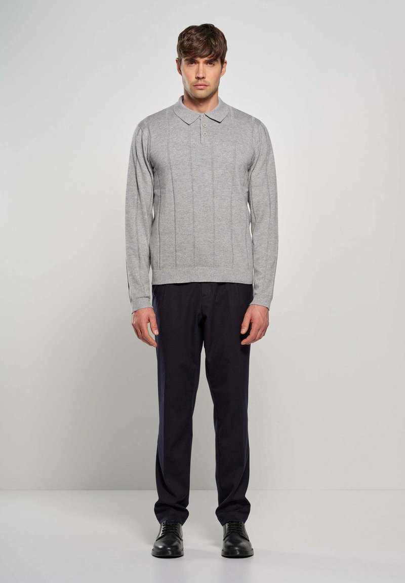 Polo grigio a maniche lunghe con texture a costine e colletto a tre bottoni, abbinato a pantaloni blu navy e scarpe nere stringate.