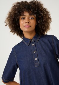 Denim shirt in een donkerblauwe kleur, met korte mouwen, een puntige kraag en vijf knopen met contrasterende stikdetails.