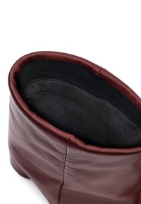 Bordeaux leren enkellaars met een zachte, zwarte binnenvoering. Beschikt over een gladde buitenkant en een nette, gebogen opening aan de bovenkant.