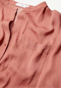 Blouse en ton pêche en tissu léger, dotée d'un col, d'une fermeture à boutons et d'une poche poitrine avec de subtils détails de couture.