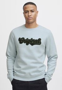 Felpa azzurra chiara con un logo nero "Original" in peluche sul davanti. Collo a giro, polsini e orlo a costine. Tessuto dalla superficie liscia.