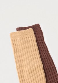 Dwie prążkowane skarpetki: jedna w jasnobeżowym kolorze, druga w ciemnym brązie. Materiał jest miękki, o fakturowanej powierzchni, z elastycznymi ściągaczami na górze.
