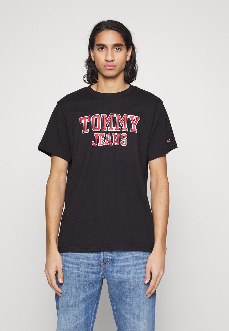 Juodas medvilninis marškinėliai su ryškiu raudonu užrašu "TOMMY JEANS" per krūtinę, trumpomis rankovėmis ir apvaliu kaklu.