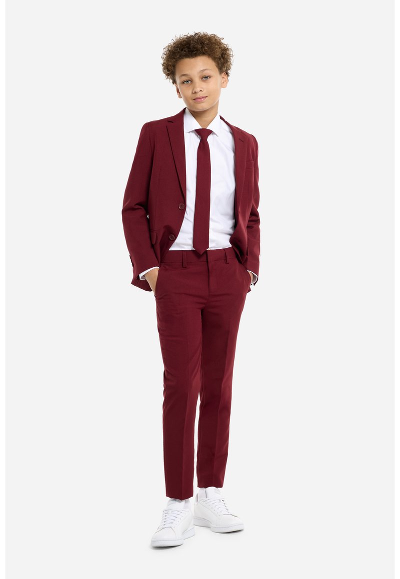 Traje burdeos con una camisa de vestir blanca y corbata a juego; presenta un corte ajustado, solapas de muesca, y está acompañado de zapatillas blancas.