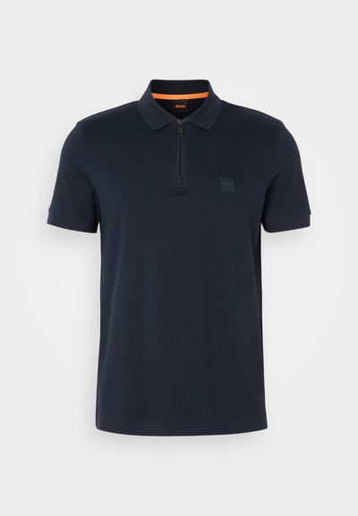 Polo shirt marine avec un col zippé, doté d'une petite écusson sur la poitrine et de manches courtes. Matière en mélange de coton avec une texture lisse.