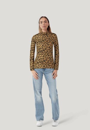 Langärmliges Top mit Stehkragen im Leopardenmuster in warmem Beige und Schwarz, kombiniert mit hellblauen geraden Jeans und weißen Sneakers.