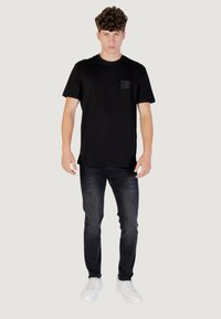 Camiseta de algodón negra de manga corta, con un pequeño bolsillo de parche negro. Combinada con jeans oscuros y zapatillas blancas.