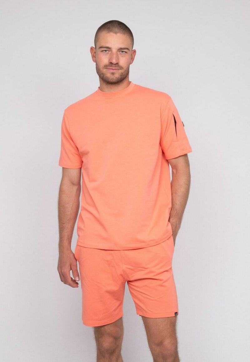 T-shirt corail à manches courtes avec un col rond, associé à un short assorti. Le tissu est lisse avec des coutures minimales et un design sportif.