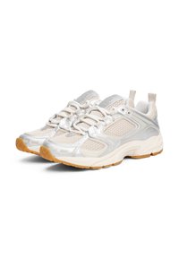 Sporty sneakers featuring a beige mesh upper, silver accents, elastic laces, and a textured gum rubber sole. Lightweight and breathable design.