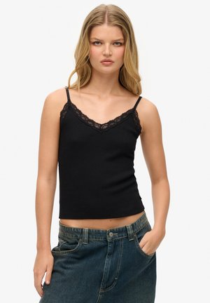 Camiseta de tirantes negra con textura acanalada y borde de encaje a lo largo del escote en V, con tirantes delgados ajustables y una forma ajustada. Llevada con jeans de talle alto.