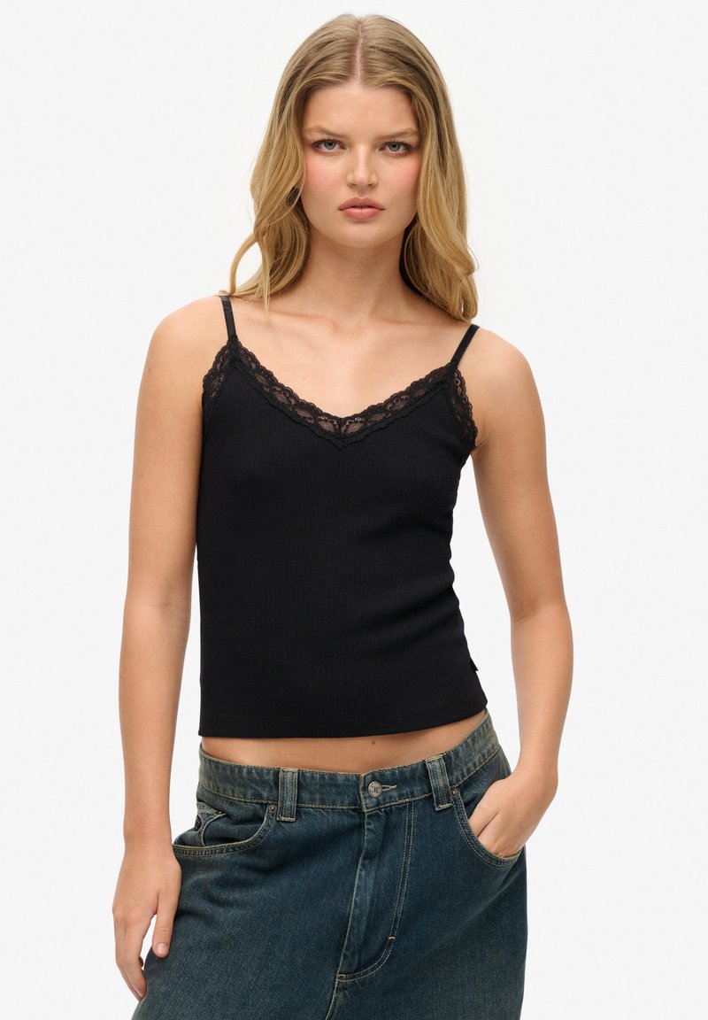 Camiseta de tirantes negra con textura acanalada y borde de encaje a lo largo del escote en V, con tirantes delgados ajustables y una forma ajustada. Llevada con jeans de talle alto.