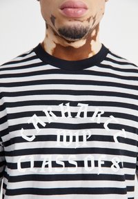 Černobílé pruhované tričko z bavlny s odvážným bílým textem "Carhartt WIP" a "Class of 8" v grafickém písmu, kulatý výstřih.