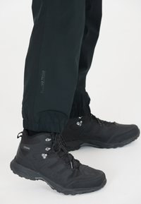 Svarta vattentäta vandringsskor med texturerade greppsålar och metallöglor för snörning, tillsammans med svarta byxor med elastiskt midjeband som har en logodetalj.