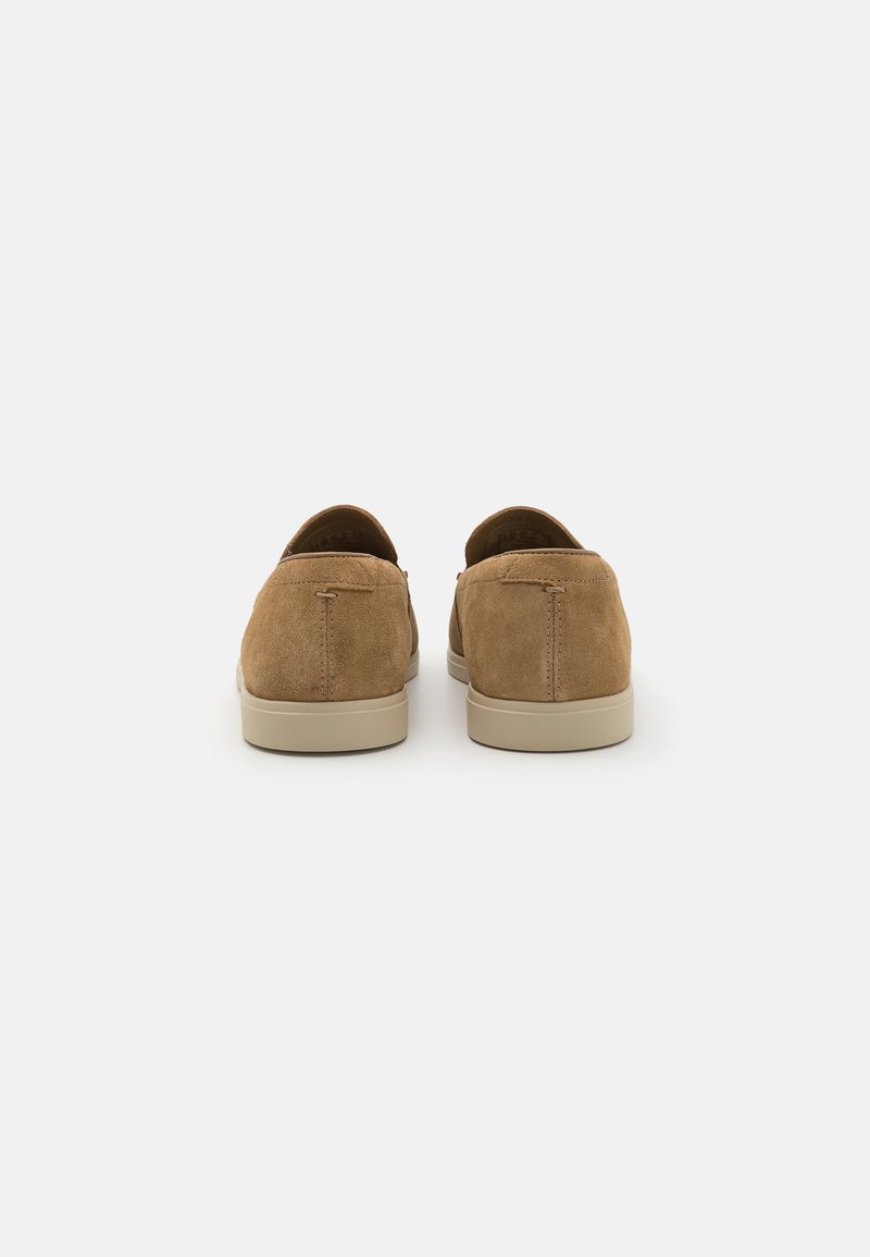 Zapatos de ante marrón tipo slip-on con un talón redondeado, que cuentan con una suela de goma beige y un sencillo detalle de costura en el tacón.