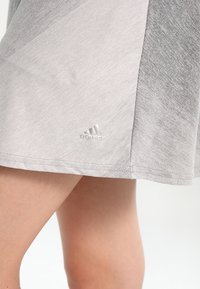 Falda deportiva gris con textura y un ligero degradado, que presenta un sutil logo de Adidas cerca del dobladillo. Tejido suave y transpirable.