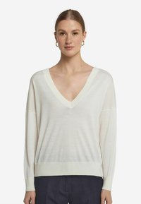 Cremfarbener V-Ausschnitt-Pullover mit langen Ärmeln und geripptem Saum. Leicht, mit weicher Textur, lockerer Passform und subtilen Nähten.