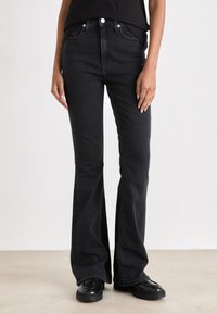 Jeans pretos de perna larga feitos de denim, com um design clássico de cinco bolsos, fecho de botão metálico e ligeiro desvitalização na bainha.