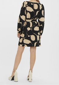 Černé šaty s abstraktními béžovými vzory, dlouhými puff rukávy, zúženým pasem a délkou po kolena. Nosí se s krémovými botami na bloku.