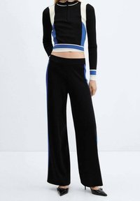 Czarny dzianinowy top o kroju crop z niebieskimi i białymi akcentami, zestawiony z czarnymi spodniami o szerokich nogawkach z niebieskimi bocznymi paskami. Gładka faktura, dopasowany krój.