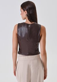 Top senza maniche in pelle marrone con un design aderente, dotato di un piccolo accento decorativo in argento sul retro e una vita elasticizzata.