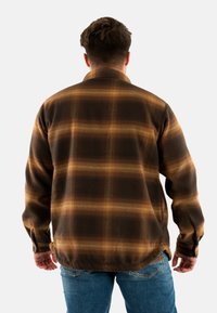 Brązowa i złota flanelowa koszula w kratę, z kołnierzykiem zapinanym na guziki, długimi rękawami i teksturowanym materiałem. Widok z tyłu ukazuje długość do talii.