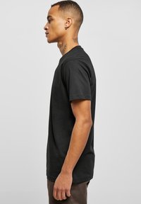 Sort bomulds t-shirt med korte ærmer og rund halsudskæring, der har en afslappet pasform og glat tekstur, båret af en person i profil.
