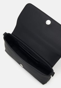 Sac à main en cuir noir avec une texture lisse, doté d'une fermeture à bouton-pression argenté et d'une forme rectangulaire élancée. L'intérieur comprend des fentes.