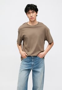 Braunes T-Shirt mit kurzen Ärmeln und lockerem Schnitt, kombiniert mit hellblauen Jeans mit geradem Bein. Schlichtes Design, weicher Stoff und entspannte Silhouette.