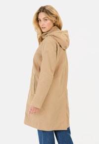Beige Kapuzenjacke mit geradem Schnitt, zwei seitlichen Taschen und einer glatten Textur. Das Design ist schlicht und weist keine auffälligen Muster auf.