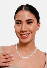 Collana di perle bianche con perle uniformi, superficie liscia e lucentezza delicata, indossata da una persona con pelle chiara e trucco minimale.