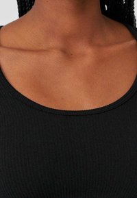 Black ribbed fabric tank top featuring a rounded neckline. Shows texture details of the material and subtle stitching along the edges.