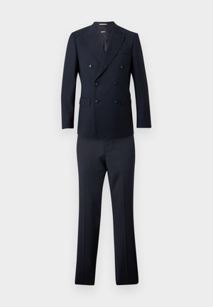 Tumši zils dubultpogājuma žakete ar sešām pogām un atbilstoši piegriezti bikses uz vienmērīga fona.