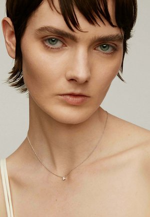 Collar de plata con un pequeño colgante de diamante sobre una fina cadena, llevado sobre piel desnuda con un brillo sutil y un diseño delicado.