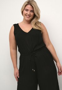 Svart ärmlös jumpsuit med V-ringning, gathered midja, dragsko i midjan och strukturerad tyg, som har en avslappnad passform och vida ben.