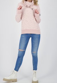 Světle růžová mikina s tečkovaným vzorem, vysokým límcem a šňůrkou. V kombinaci s roztrhanými modrými džíny a bílými šněrovacími botami.