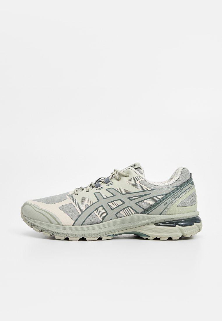 Baskets de course ASICS gris clair et beige avec un logo gris foncé et une semelle rembourrée, vues de côté sur fond blanc.