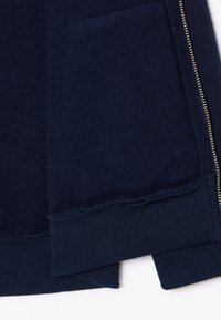 Μπλε ναυτικό φούτερ με απαλή υφή, ριμπ μανσέτες και λεπτομέρεια χρυσού φερμουάρ στην πλευρά για εύκολο κλείσιμο.