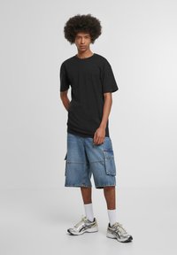 Camiseta negra de manga corta con un ajuste relajado, combinada con pantalones cortos de cargo azules que cuentan con múltiples bolsillos y un acabado de mezclilla deslavado. Zapatillas deportivas plateadas.